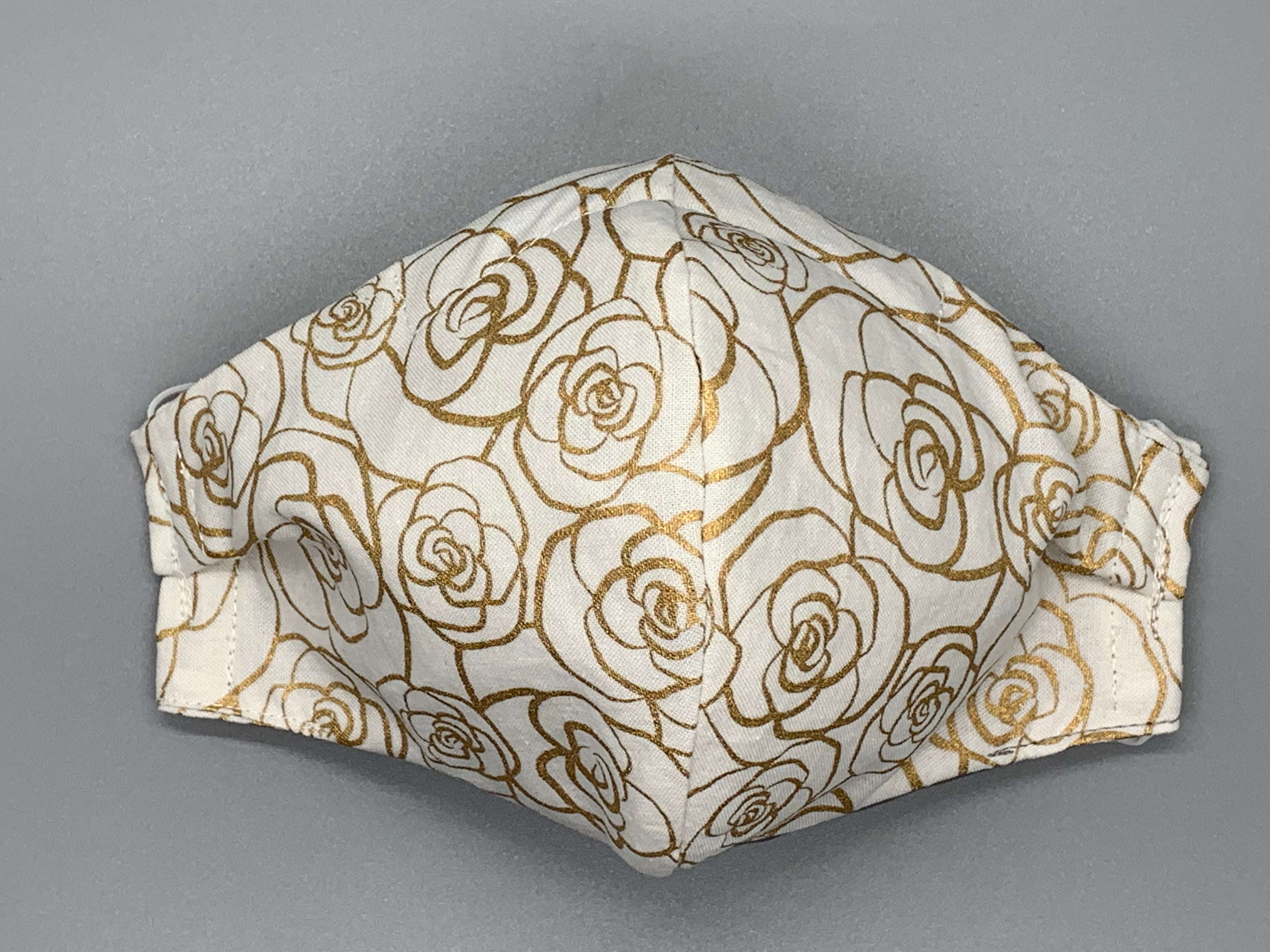 Handmade Triple Layer Cotton Facemask. Gold outline roses on white cotton. Fabric enclosed nose wire. Gray filter pocket. Comfy adjustable white elastic earloops. Cut from one cloth-meaning fabric is same and where your pattern lies may vary. non-returnable/non-refundable. non medical grade. not a replacement for medical grade personal protective equipment (PPE), surgical masks, N95s, or social distancing. follow all recommended CDC guidelines.