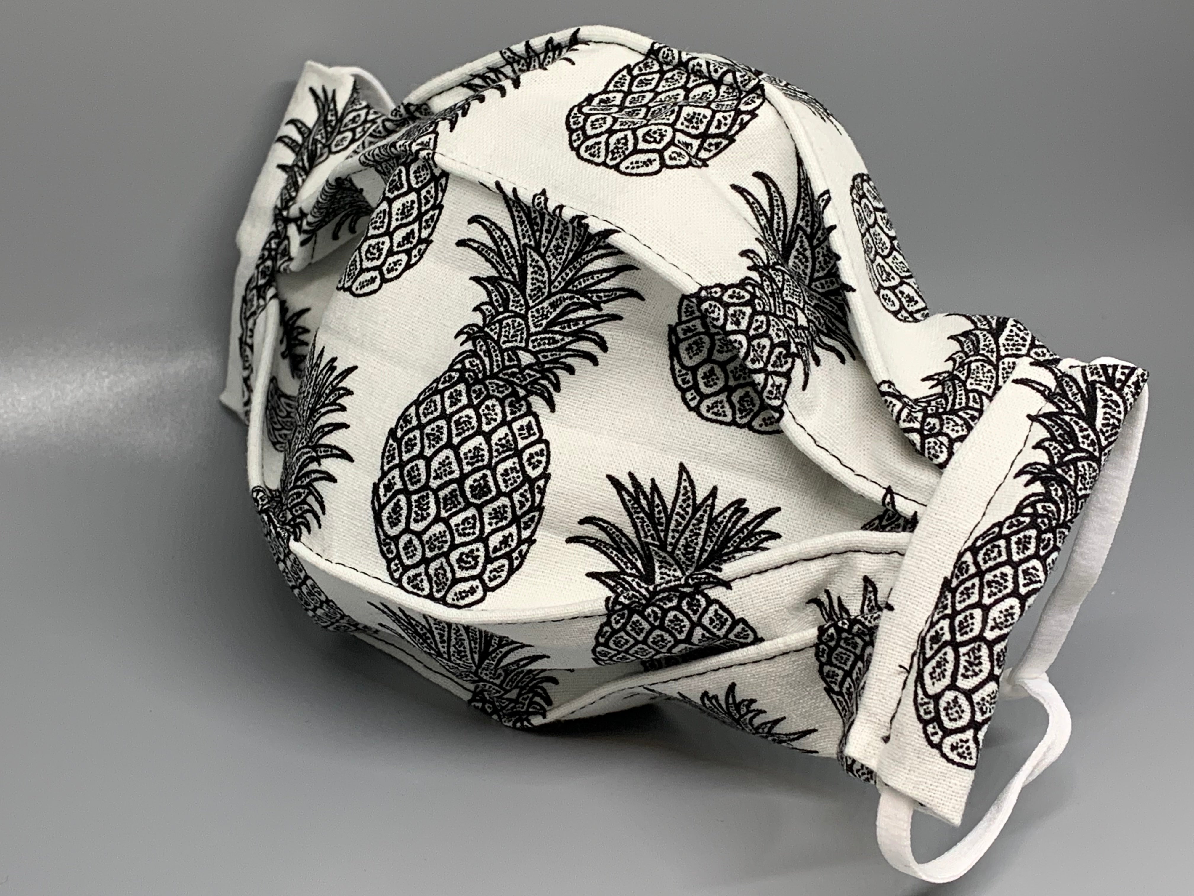 Handmade Triple Layer Cotton Facemask. Pineapples drawn in black on white cotton, accordion style mask. Fabric enclosed nose wire. Comfy adjustable white elastic earloops. This mask has no filter pocket.  Cut from one cloth-meaning fabric is same and where your pattern lies may vary. non-returnable/non-refundable. non medical grade. not a replacement for medical grade personal protective equipment (PPE), surgical masks, N95s, or social distancing. Follow all recommended CDC guidelines.