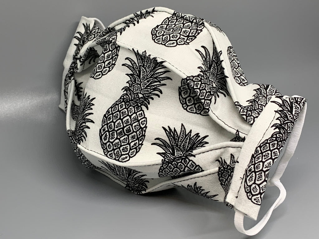 Handmade Triple Layer Cotton Facemask. Pineapples drawn in black on white cotton, accordion style mask. Fabric enclosed nose wire. Comfy adjustable white elastic earloops. This mask has no filter pocket.  Cut from one cloth-meaning fabric is same and where your pattern lies may vary. non-returnable/non-refundable. non medical grade. not a replacement for medical grade personal protective equipment (PPE), surgical masks, N95s, or social distancing. Follow all recommended CDC guidelines.