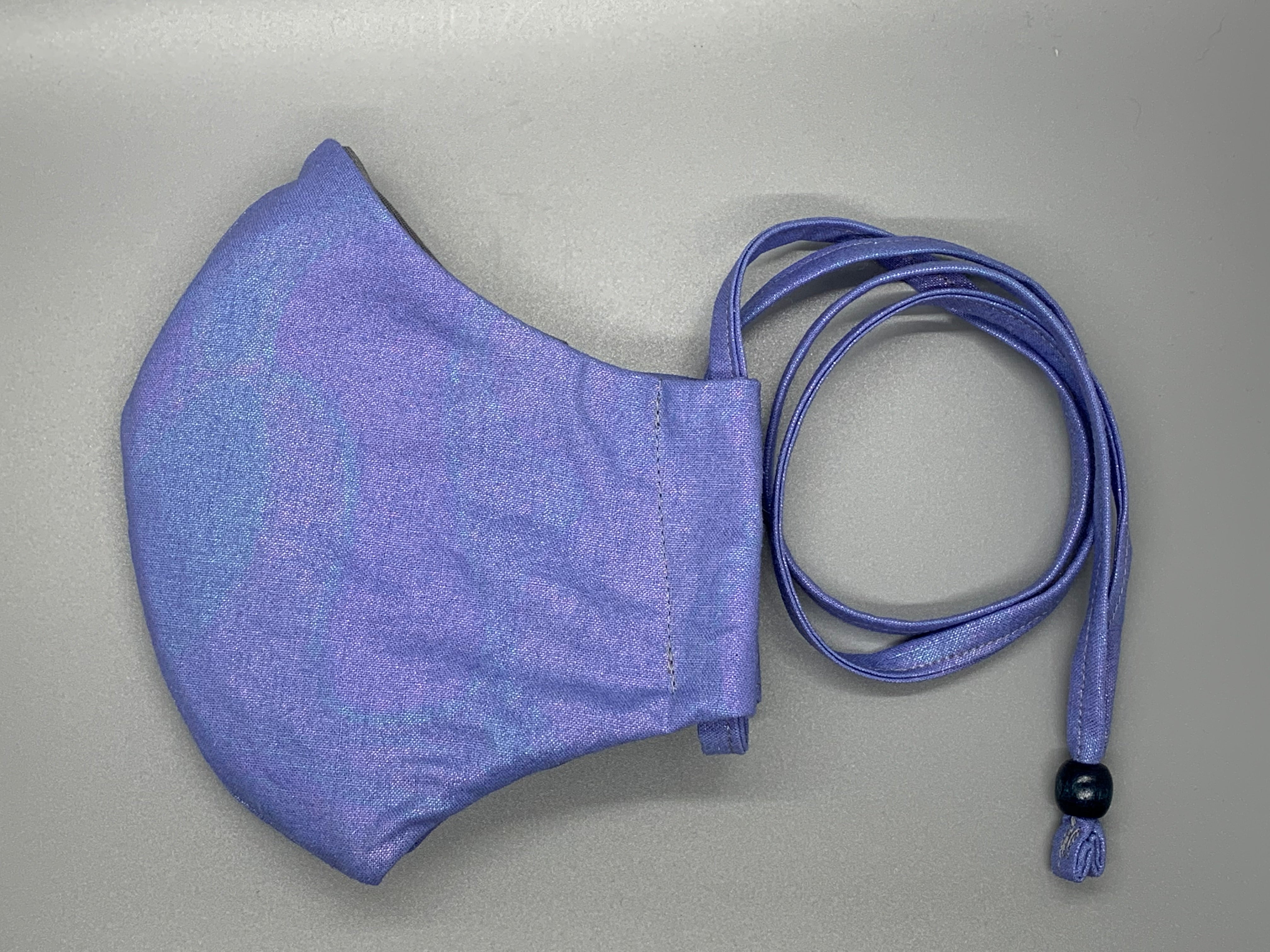 Handmade Triple Layer Cotton Facemask. Dreamy Irridescent purple ombre cotton. Fabric enclosed nose wire. Gray filter pocket. Overhead/Back of Head cotton loop from same fabric. Adjustable Wood Bead for perfect fit. This mask has no nose wire-the adjustable overhead loop gives you a snug fit. Cut from one cloth-meaning fabric is same and where your pattern lies may vary. non-returnable/non-refundable. non medical grade. not a replacement for medical grade personal protective equipment (PPE), surgical masks,