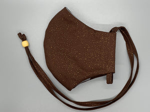  Handmade Triple Layer Cotton Facemask. Melanin brown cotton covered in gold flecks. Gray filter pocket. Overhead/Back of Head cotton loop from same fabric. Adjustable Wood Bead for perfect fit. This mask has no nose wire-the adjustable overhead loop gives you a snug fit. Cut from one cloth-meaning fabric is same and where your pattern lies may vary. non-returnable/non-refundable. non medical grade. not a replacement for medical grade personal protective equipment (PPE), surgical masks, N95s, or social dist