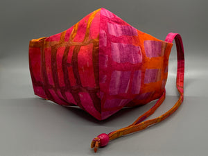 Takes me back to Hawaii's fiery sunsets.  Hues of purple and orange with rectangle shapes throughout. Gray filter pocket. Overhead/Back of Head cotton loop from same fabric. Adjustable Wood Bead for perfect fit. This mask has no nose wire-the adjustable overhead loop gives you a snug fit.