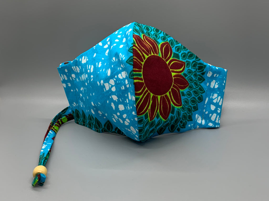 Lay down in a sunflower field on a cloudless day. This African wax cloth features maroon sunflower, green petals, bright blue, and white. Gray filter pocket. Overhead/Back of Head cotton loop from same fabric. Adjustable Wood Bead for perfect fit. This mask has no nose wire-the adjustable overhead loop gives you a snug fit.