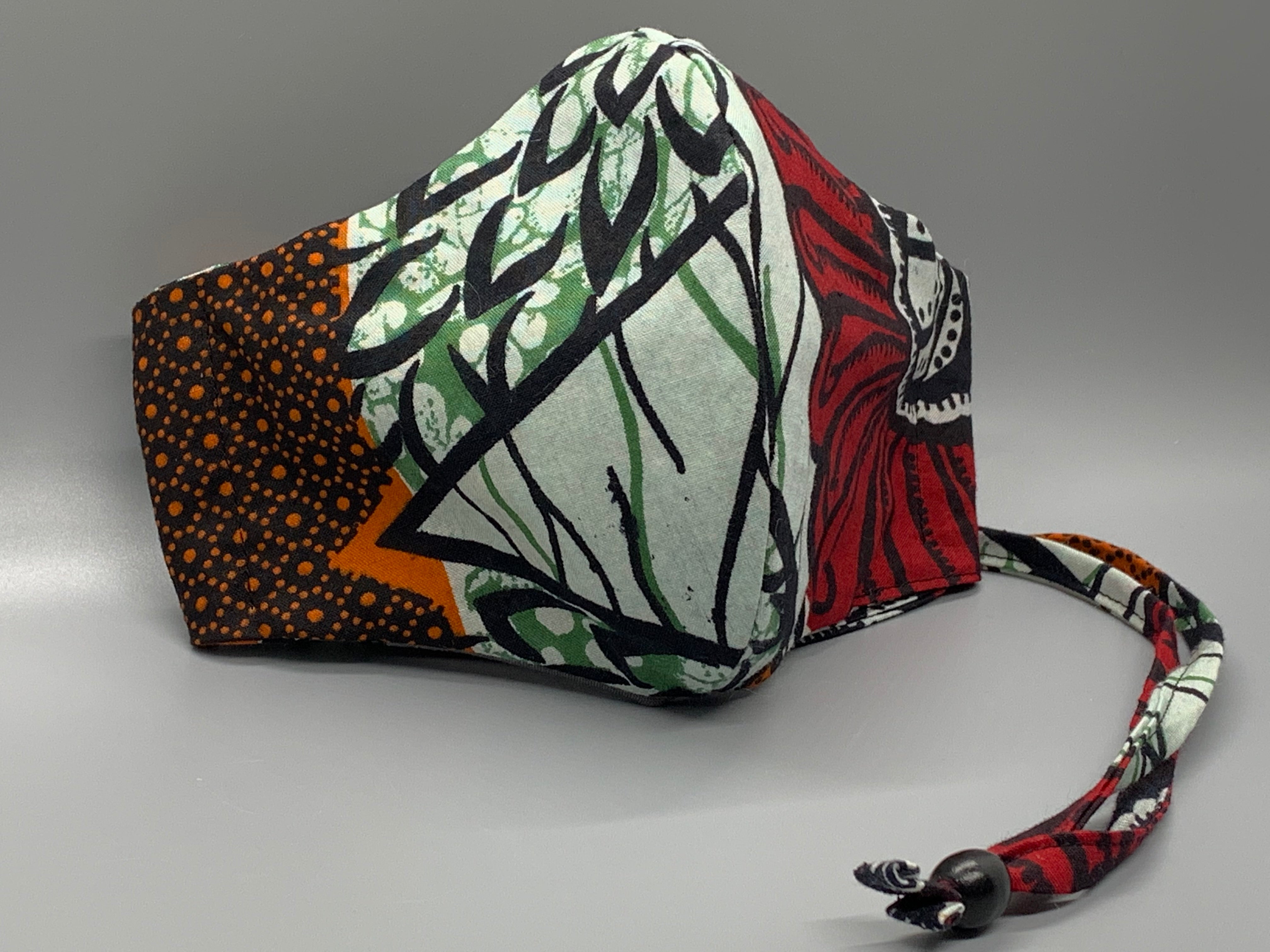 Cool green and black vine with orange, foam, green, and red pattern. Gray filter pocket. Overhead/Back of Head cotton loop from same fabric. Adjustable Wood Bead for perfect fit. This mask has no nose wire-the adjustable overhead loop gives you a snug fit.  Cut from one cloth-meaning fabric is same and where your pattern lies may vary. non-returnable/non-refundable. non medical grade. 