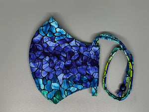 A gorgeous purple to yellow ( with turquoise, blue, and green) ombre across an almost stain glassed black pattern outline. Gray filter pocket. Overhead/Back of Head cotton loop from same fabric. Adjustable Wood Bead for perfect fit. This mask has no nose wire-the adjustable overhead loop gives you a snug fit.