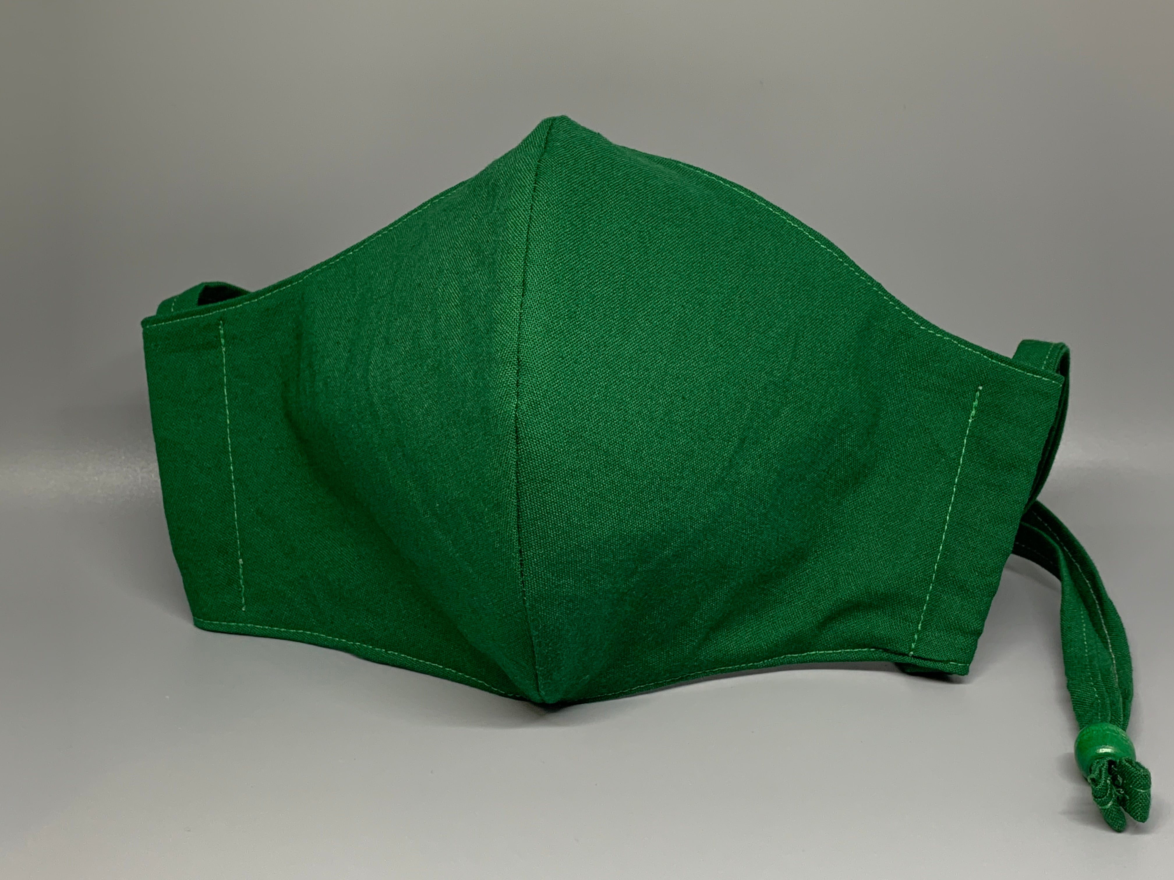 Vibrant solid green cotton. Gray filter pocket. Overhead/Back of Head cotton loop from same fabric. Adjustable Wood Bead for perfect fit. This mask has no nose wire-the adjustable overhead loop gives you a snug fit.