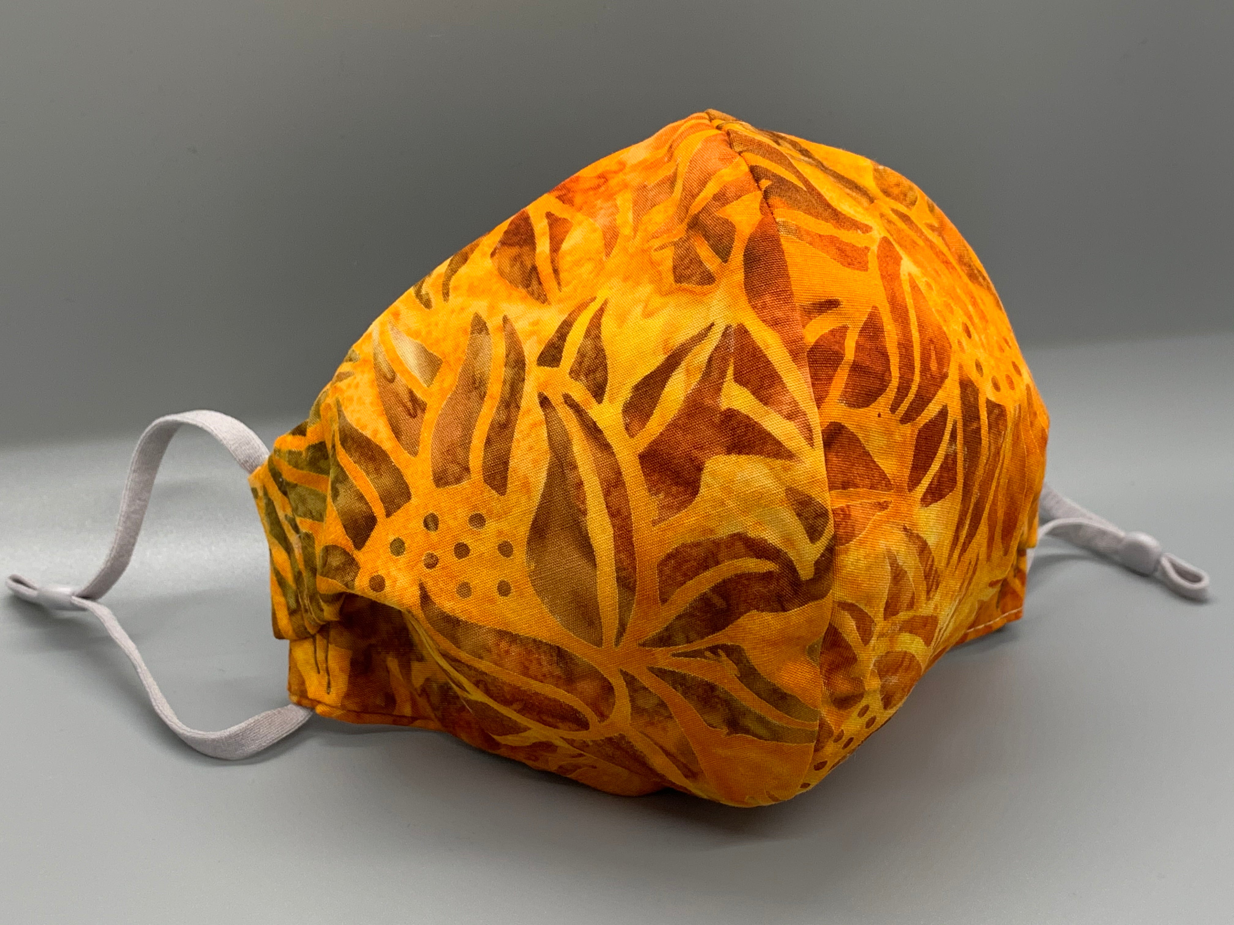 Handmade triple layer cotton facemask. Fiery sunflowers on batik orange cotton. Gray filter pocket. Fabric enclosed nose wire. Comfy adjustable gray elastic earloops.