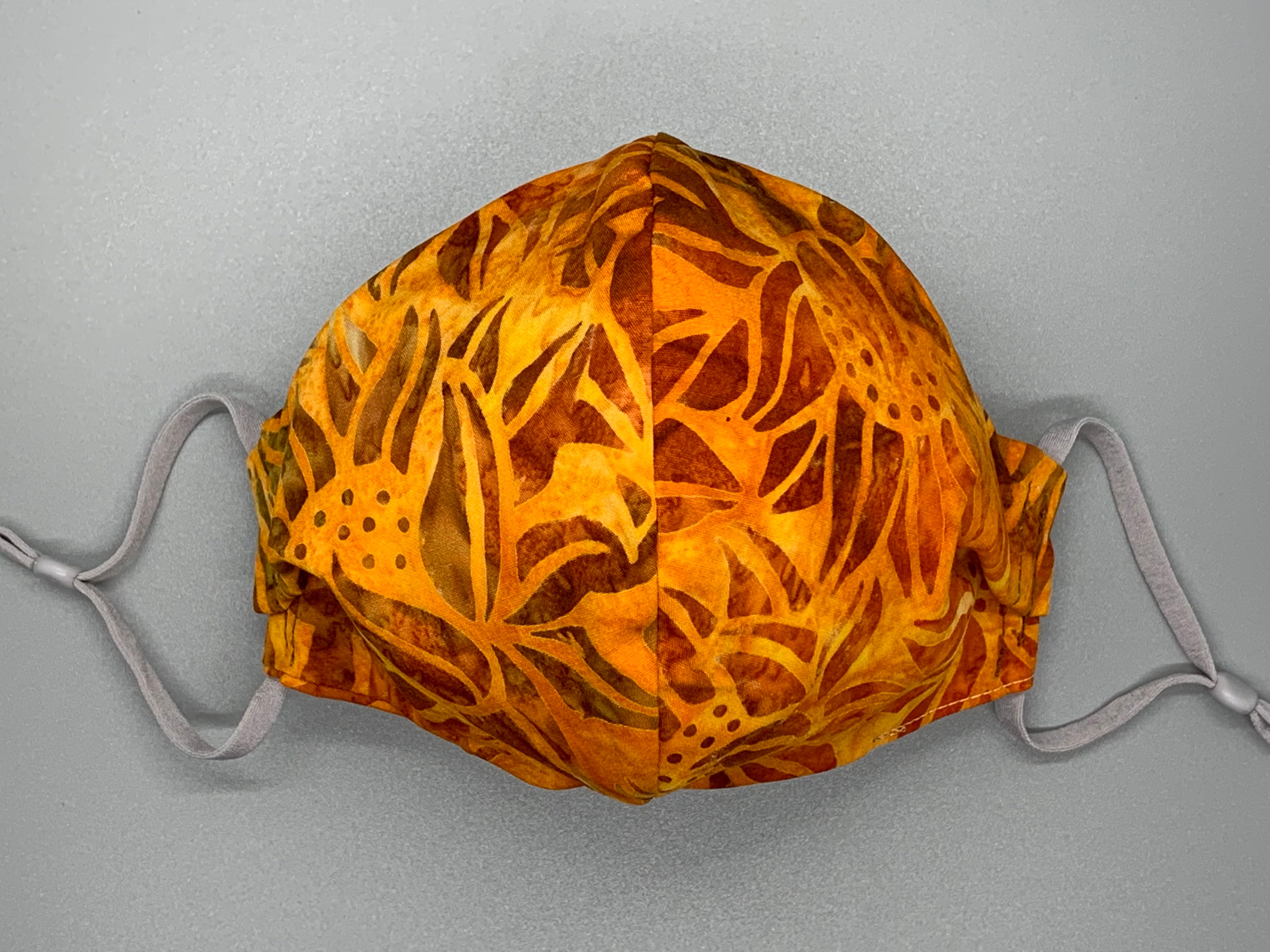 Handmade triple layer cotton facemask. Fiery sunflowers on batik orange cotton. Gray filter pocket. Fabric enclosed nose wire. Comfy adjustable gray elastic earloops.