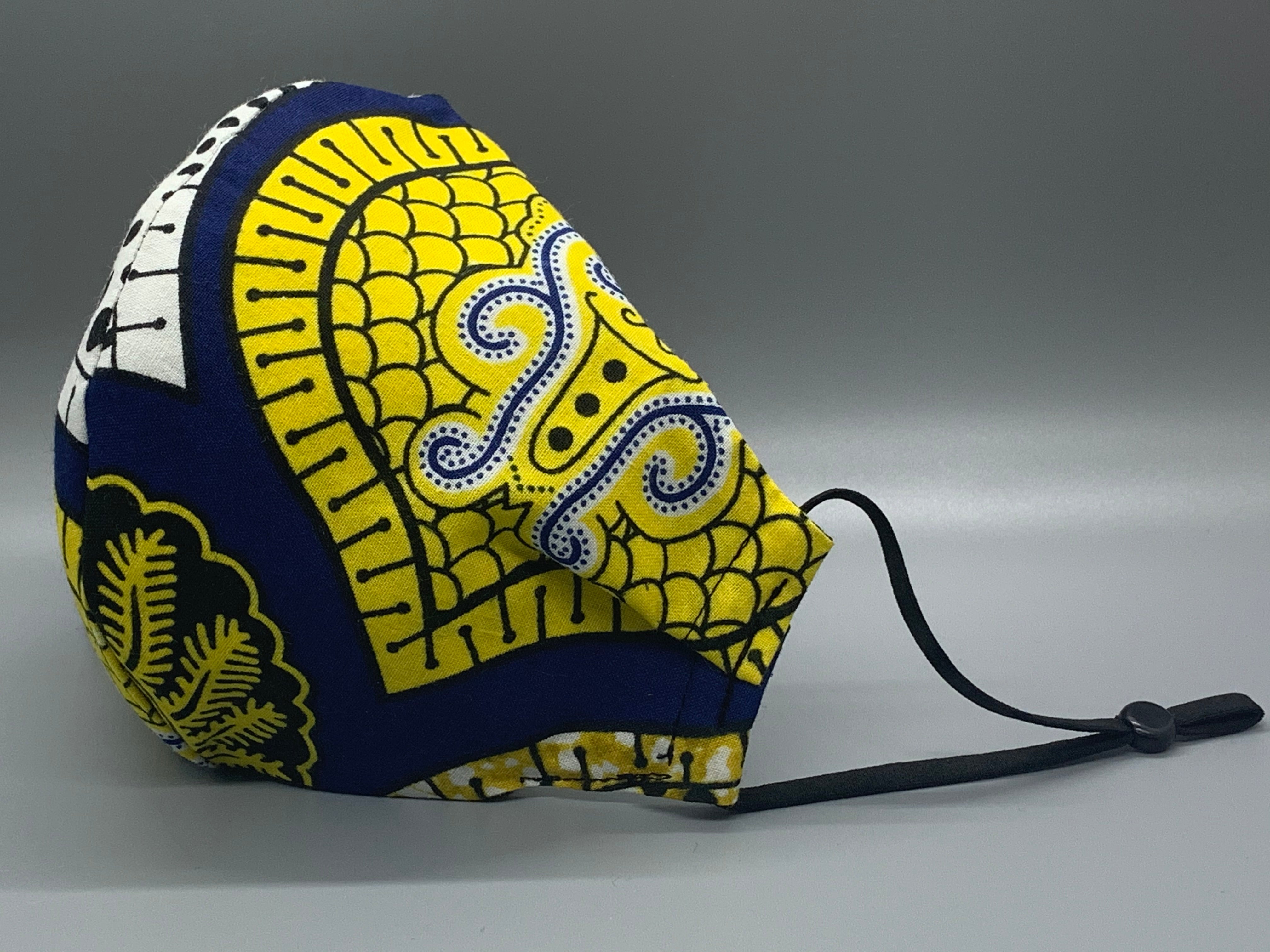 Handmade triple layer cotton facemask. Gorgeous blue, fabric with symbols/pattern in yellow white and black. The ream stated this fabric is from Ghana (or inspired by their amazing prints). Fabric enclosed nose wire. Grey filter pocket. Comfy adjustable black elastic ear loops.  Edit alt text