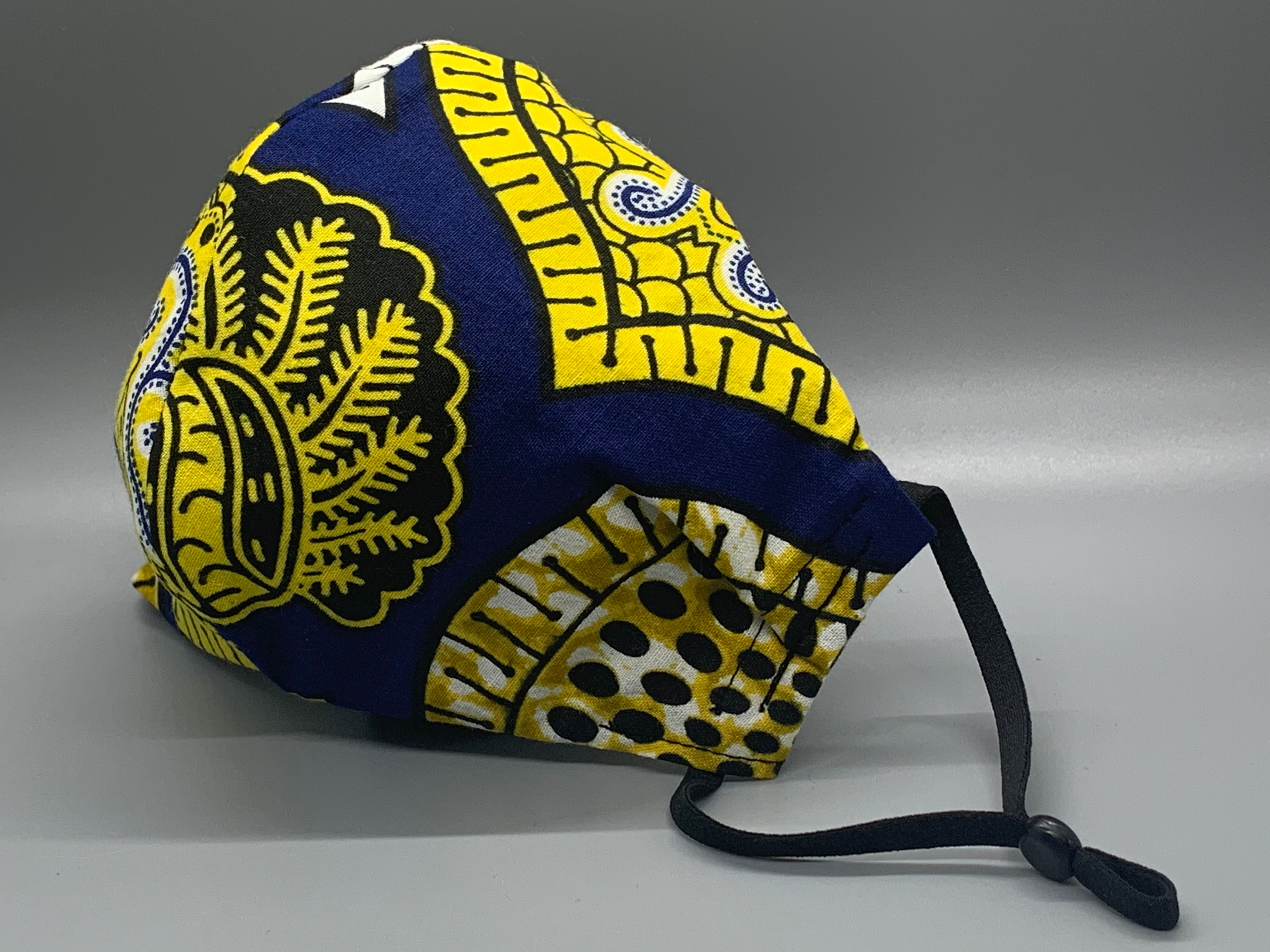 Handmade triple layer cotton facemask. Gorgeous blue, fabric with symbols/pattern in yellow white and black. The ream stated this fabric is from Ghana (or inspired by their amazing prints). Fabric enclosed nose wire. Grey filter pocket. Comfy adjustable black elastic ear loops.